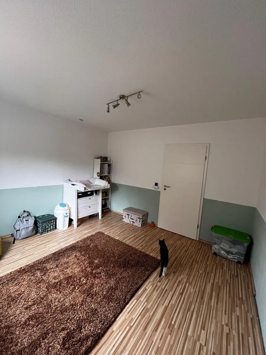 Vorher: karger Raum mit weißer Wickelkommode und schlichtem salbeigrünem Farbstreifen an der Wand